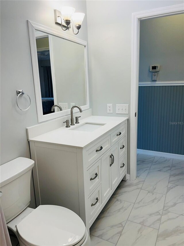 half bathroom featuring vanity, toilet, and marble finish floor