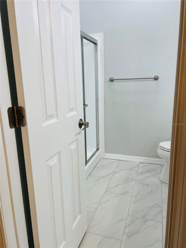 bathroom featuring toilet and a shower with shower door