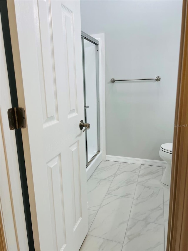 bathroom featuring toilet, baseboards, marble finish floor, and a stall shower