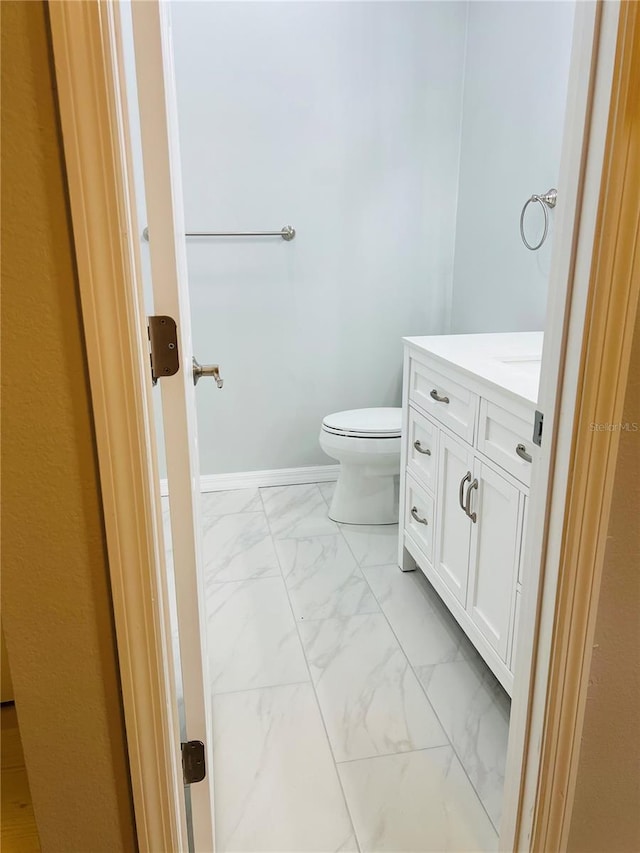 half bath with vanity, toilet, baseboards, and marble finish floor