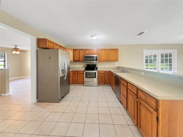 kitchen featuring stainless steel appliances, kitchen peninsula, light tile patterned floors, and sink