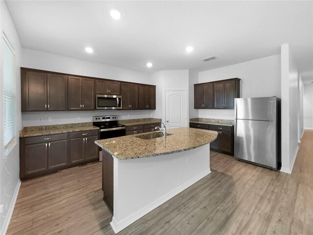 kitchen featuring hardwood / wood-style flooring, light stone countertops, stainless steel appliances, sink, and dark brown cabinets