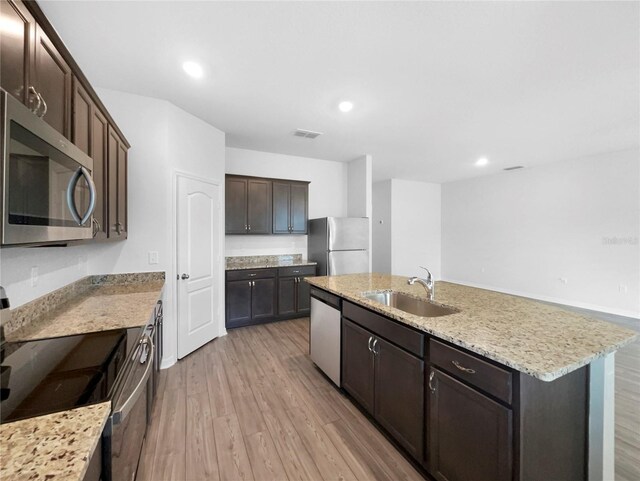 kitchen featuring light hardwood / wood-style flooring, light stone counters, stainless steel appliances, sink, and an island with sink