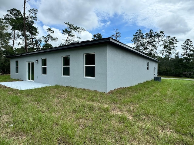 view of side of property with a lawn, a patio, and central AC