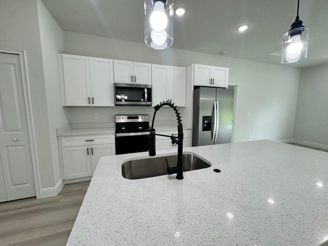 kitchen featuring light stone countertops, light hardwood / wood-style floors, hanging light fixtures, stainless steel appliances, and white cabinets