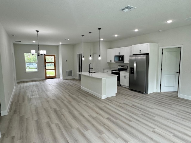 kitchen with stainless steel appliances, an inviting chandelier, an island with sink, sink, and light hardwood / wood-style floors