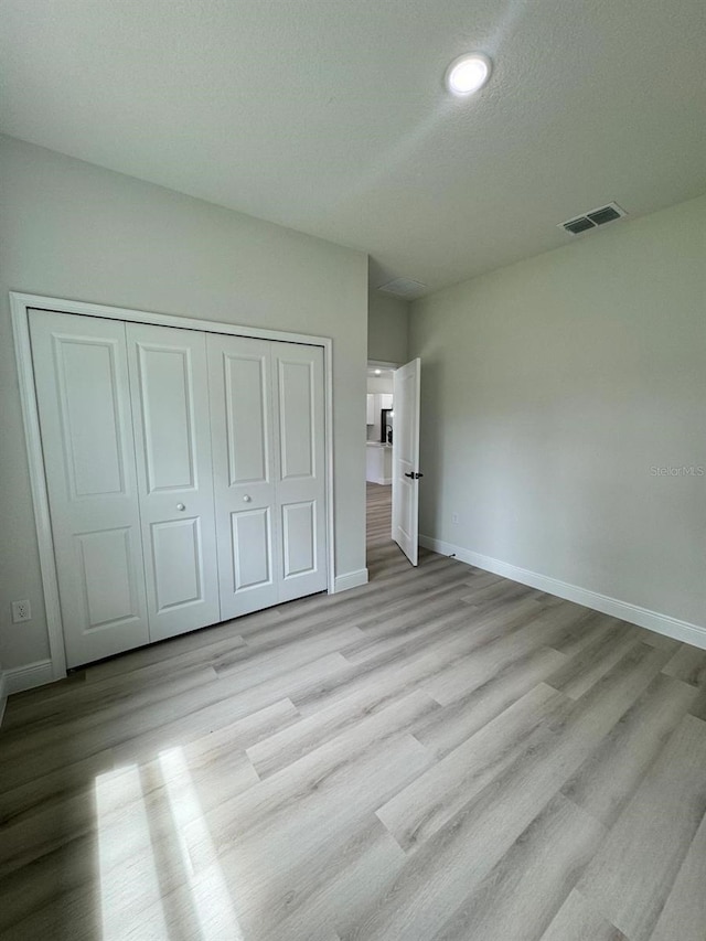 unfurnished bedroom with a closet, light hardwood / wood-style floors, and a textured ceiling