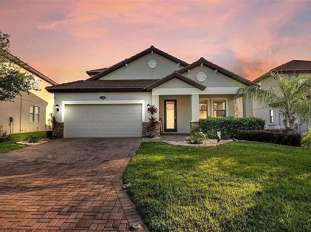 view of front facade featuring stucco siding, decorative driveway, a garage, and a yard