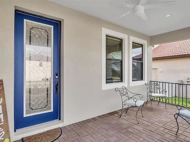 entrance to property with stucco siding, a porch, and a ceiling fan