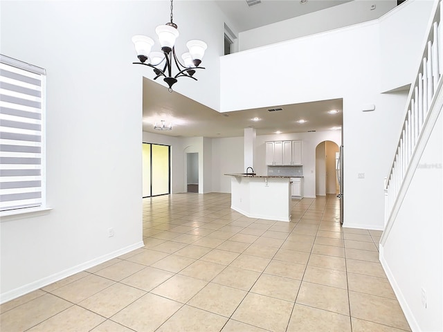 unfurnished living room with a towering ceiling, sink, light tile patterned floors, and a notable chandelier