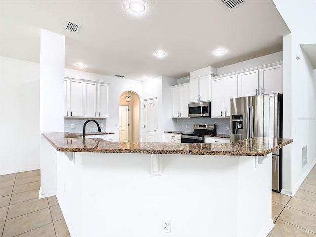 kitchen with appliances with stainless steel finishes, sink, kitchen peninsula, dark stone counters, and tasteful backsplash