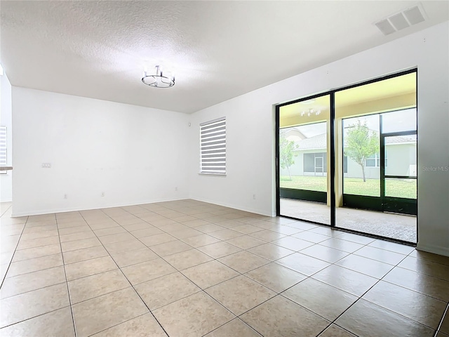 spare room with an inviting chandelier, a textured ceiling, and light tile patterned floors