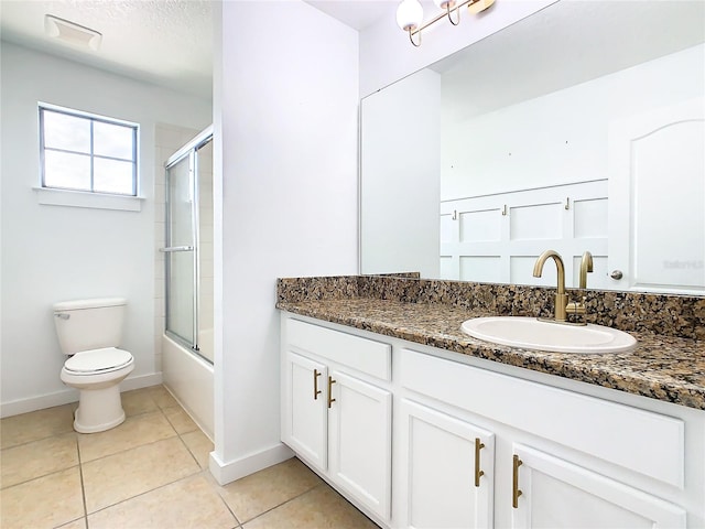 full bathroom with a textured ceiling, vanity, combined bath / shower with glass door, tile patterned flooring, and toilet