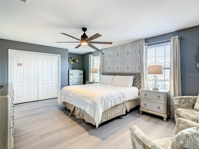 bedroom with multiple windows, light hardwood / wood-style floors, ceiling fan, and a closet