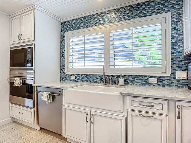 kitchen with light stone countertops, appliances with stainless steel finishes, crown molding, sink, and light wood-type flooring