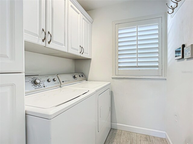 clothes washing area with washing machine and clothes dryer, cabinets, and light wood-type flooring