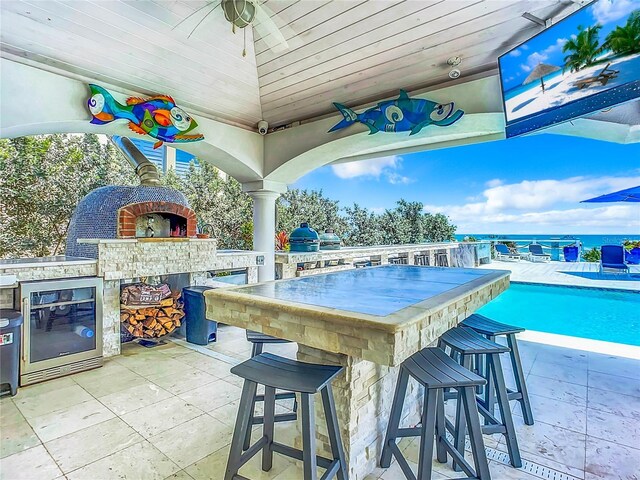 view of patio / terrace featuring a water view, an outdoor fireplace, an outdoor kitchen, wine cooler, and an outdoor bar