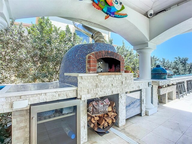 view of patio with exterior kitchen, an outdoor stone fireplace, and wine cooler