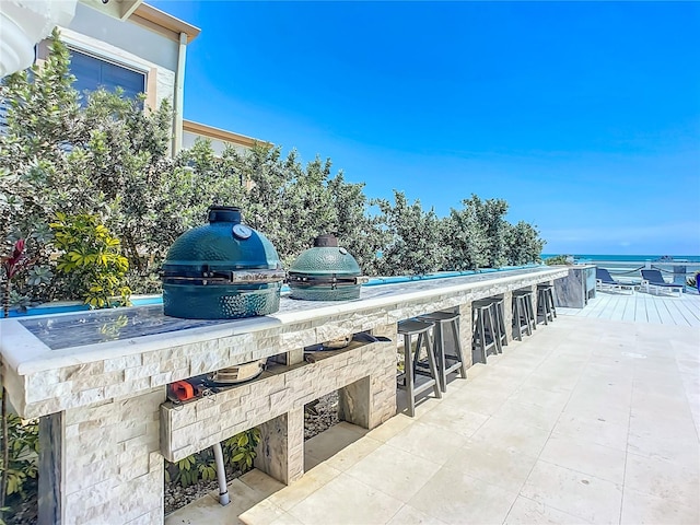 view of patio featuring exterior kitchen, a water view, and an outdoor bar