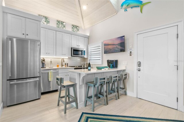 kitchen featuring light wood-type flooring, high vaulted ceiling, a kitchen bar, stainless steel appliances, and kitchen peninsula