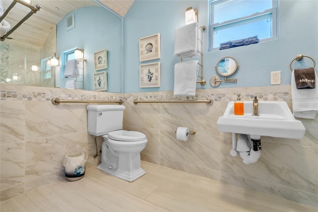 bathroom with tile walls, toilet, a wealth of natural light, and vaulted ceiling