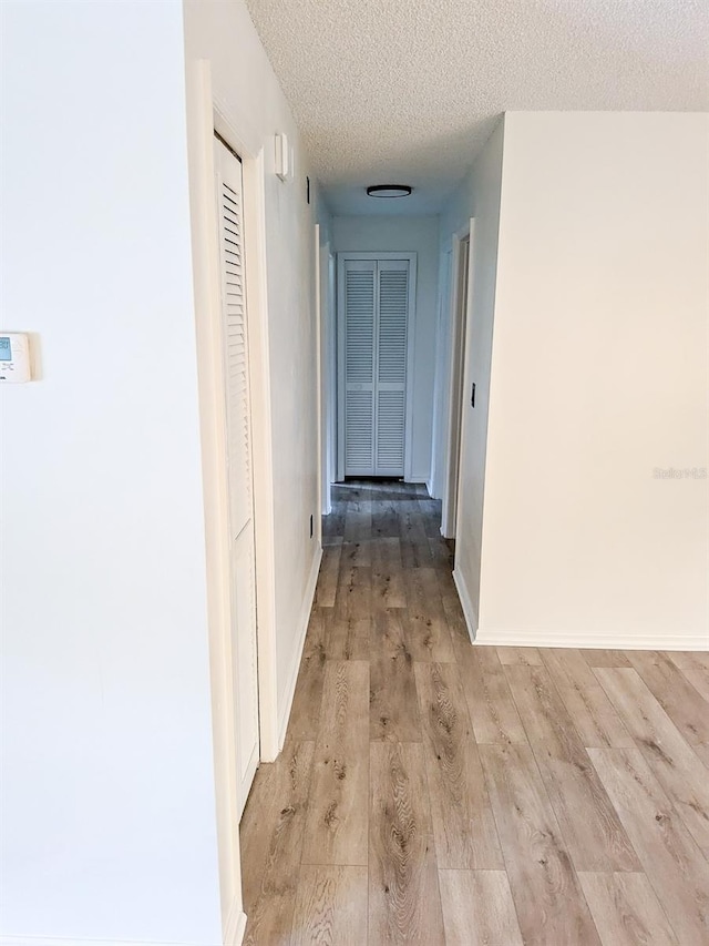 corridor with light wood-type flooring and a textured ceiling