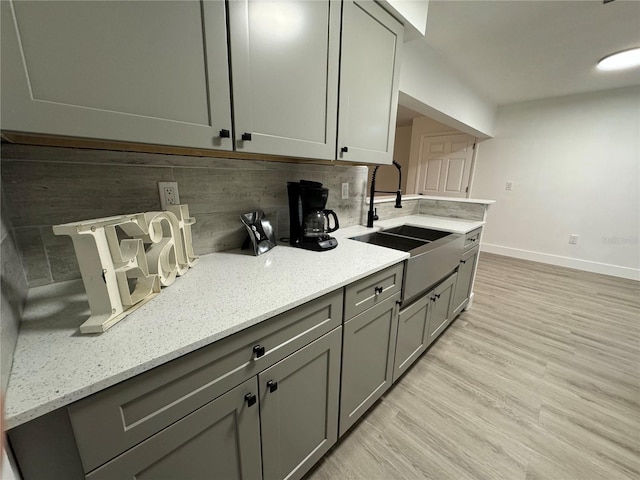 kitchen featuring backsplash, light stone counters, sink, gray cabinets, and light hardwood / wood-style floors