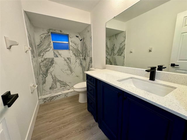 bathroom featuring wood-type flooring, vanity, a tile shower, and toilet