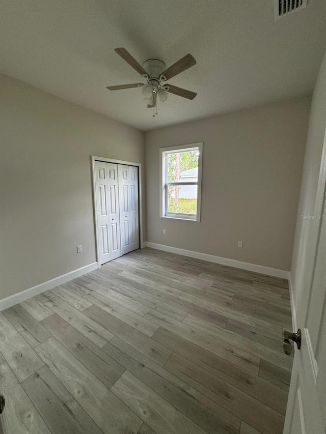 unfurnished bedroom featuring light wood-type flooring, a textured ceiling, ceiling fan, and a closet