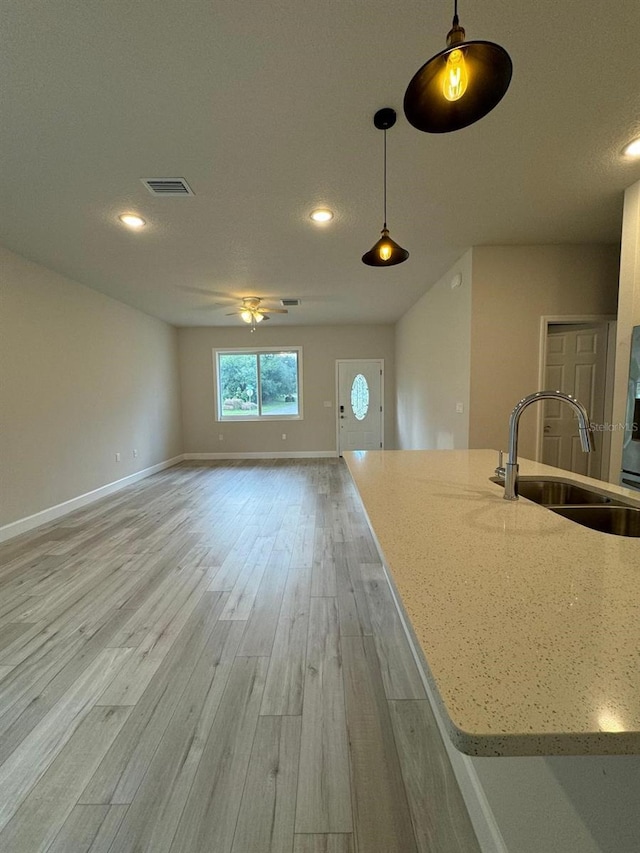 kitchen featuring light hardwood / wood-style flooring, pendant lighting, light stone countertops, and sink