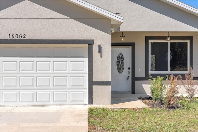 property entrance featuring a porch, concrete driveway, an attached garage, and stucco siding