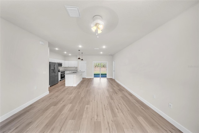 unfurnished living room featuring light wood-style flooring, a sink, a ceiling fan, visible vents, and baseboards