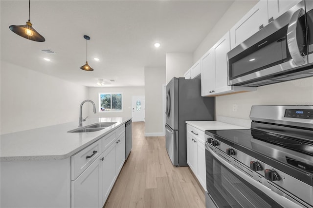 kitchen with decorative light fixtures, stainless steel appliances, light countertops, white cabinetry, and a sink