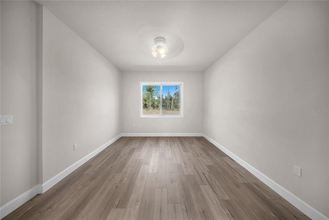 empty room featuring a textured ceiling, baseboards, and wood finished floors