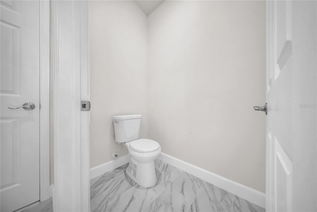 bathroom with toilet, marble finish floor, and baseboards