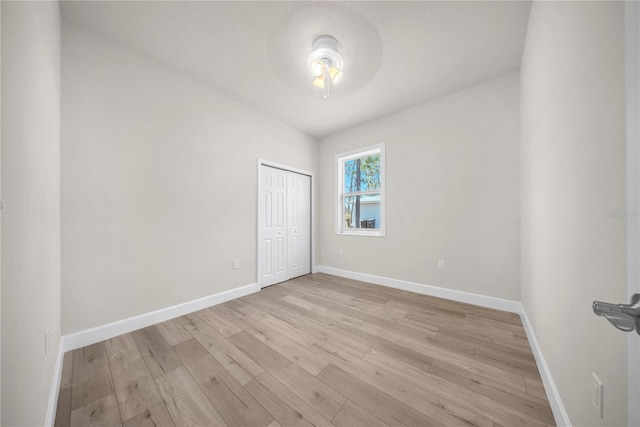 unfurnished bedroom featuring light wood finished floors, baseboards, and a closet