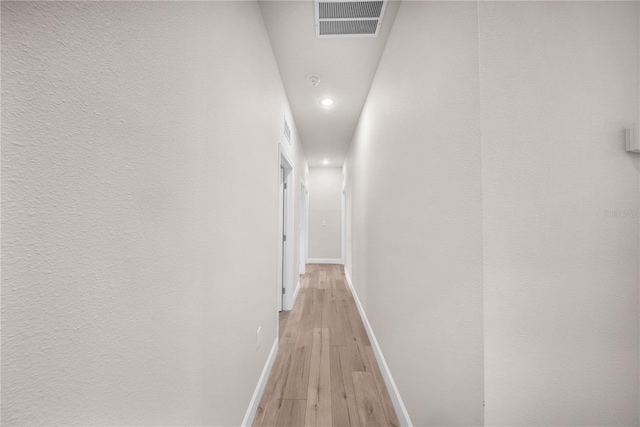 hallway featuring light wood finished floors, visible vents, and baseboards