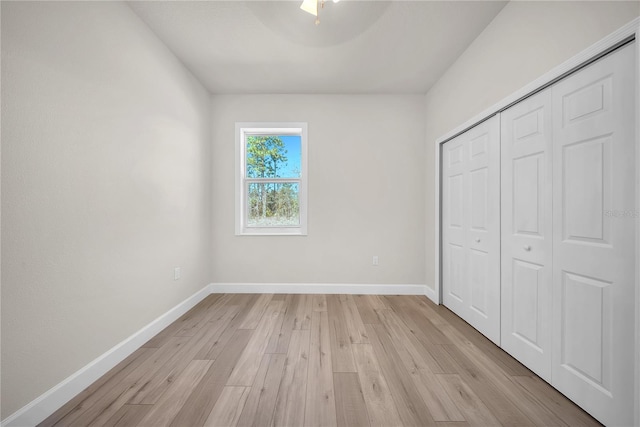 unfurnished bedroom with ceiling fan, a closet, light wood-style flooring, and baseboards