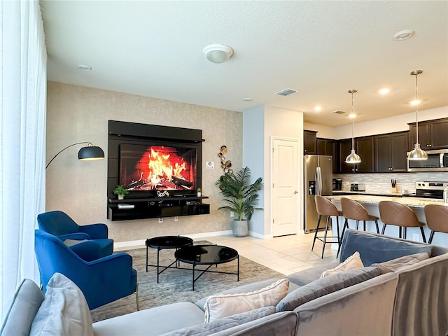 living area with light tile patterned floors, visible vents, baseboards, and a lit fireplace