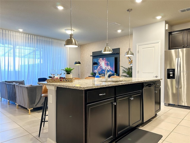 kitchen featuring stainless steel fridge, decorative light fixtures, light stone counters, sink, and a center island with sink