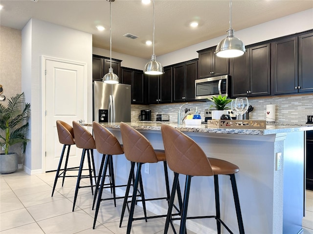 kitchen with appliances with stainless steel finishes, light stone countertops, pendant lighting, and a breakfast bar