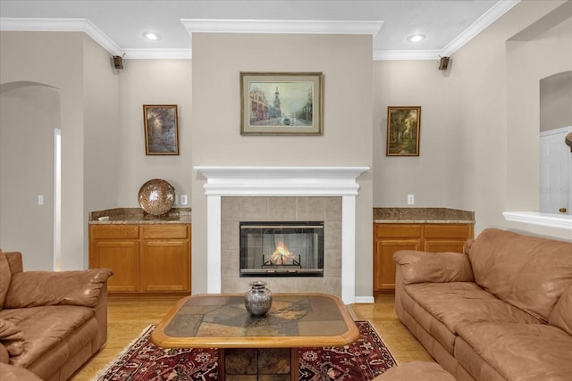 living room with a tile fireplace, crown molding, and light hardwood / wood-style flooring