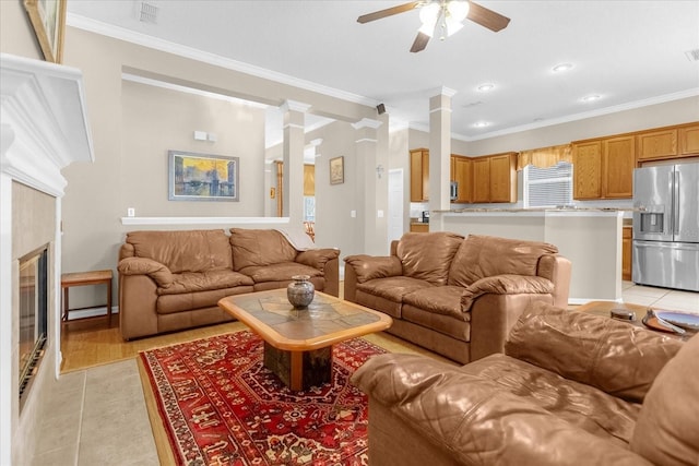 tiled living room with decorative columns, crown molding, a fireplace, and ceiling fan