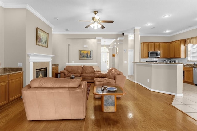 living room featuring ceiling fan, light hardwood / wood-style floors, ornamental molding, and a tiled fireplace