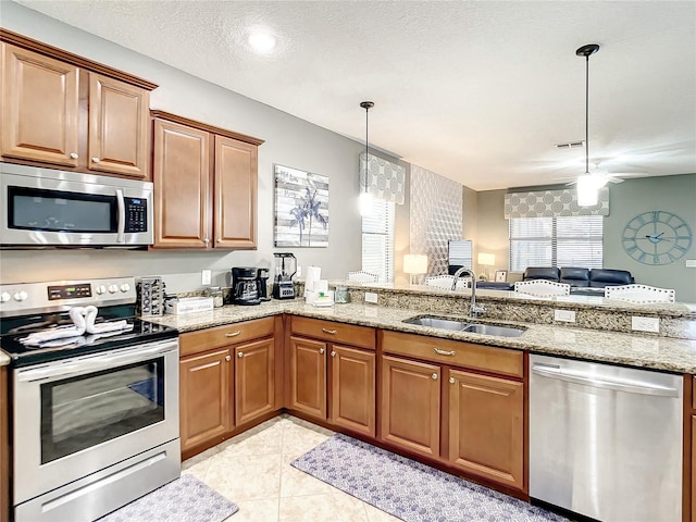 kitchen featuring stainless steel appliances, sink, light stone countertops, and kitchen peninsula