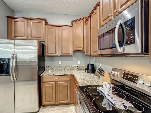 kitchen featuring a textured ceiling, light stone counters, and stainless steel appliances