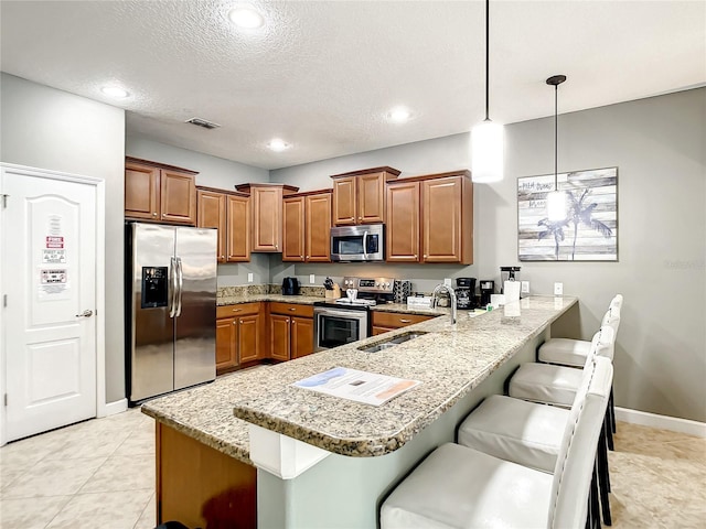 kitchen with a kitchen breakfast bar, pendant lighting, stainless steel appliances, sink, and kitchen peninsula