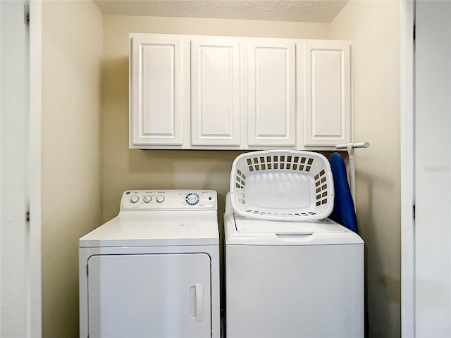 clothes washing area with washer and dryer, cabinets, and a textured ceiling