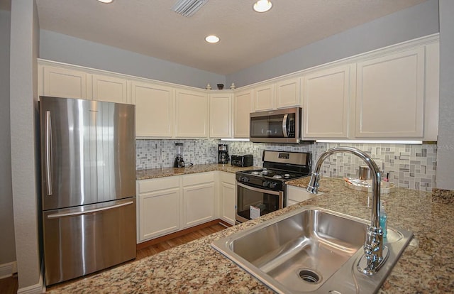 kitchen with light stone countertops, backsplash, wood-type flooring, stainless steel appliances, and sink