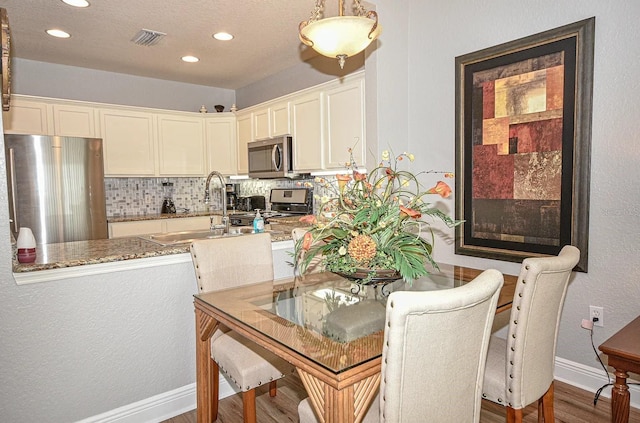 kitchen featuring hardwood / wood-style floors, tasteful backsplash, stainless steel appliances, sink, and light stone countertops